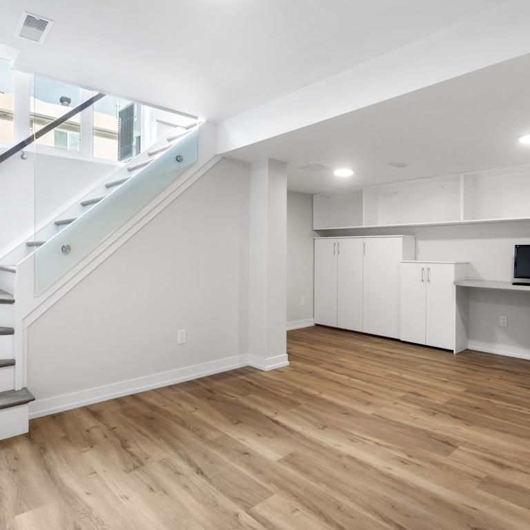 an empty room with a desk, computer, and stairs